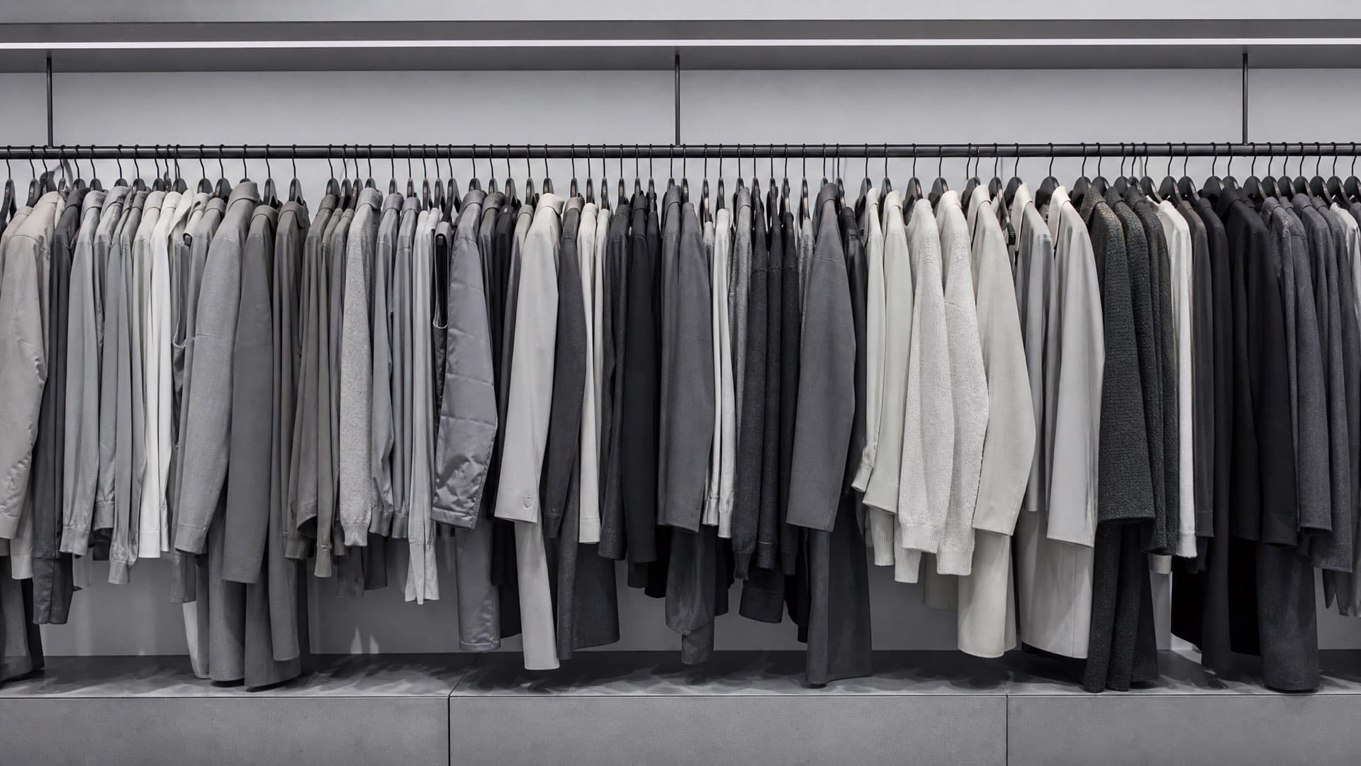 A dense rail of neutral-coloured garments in a cool-lit interior