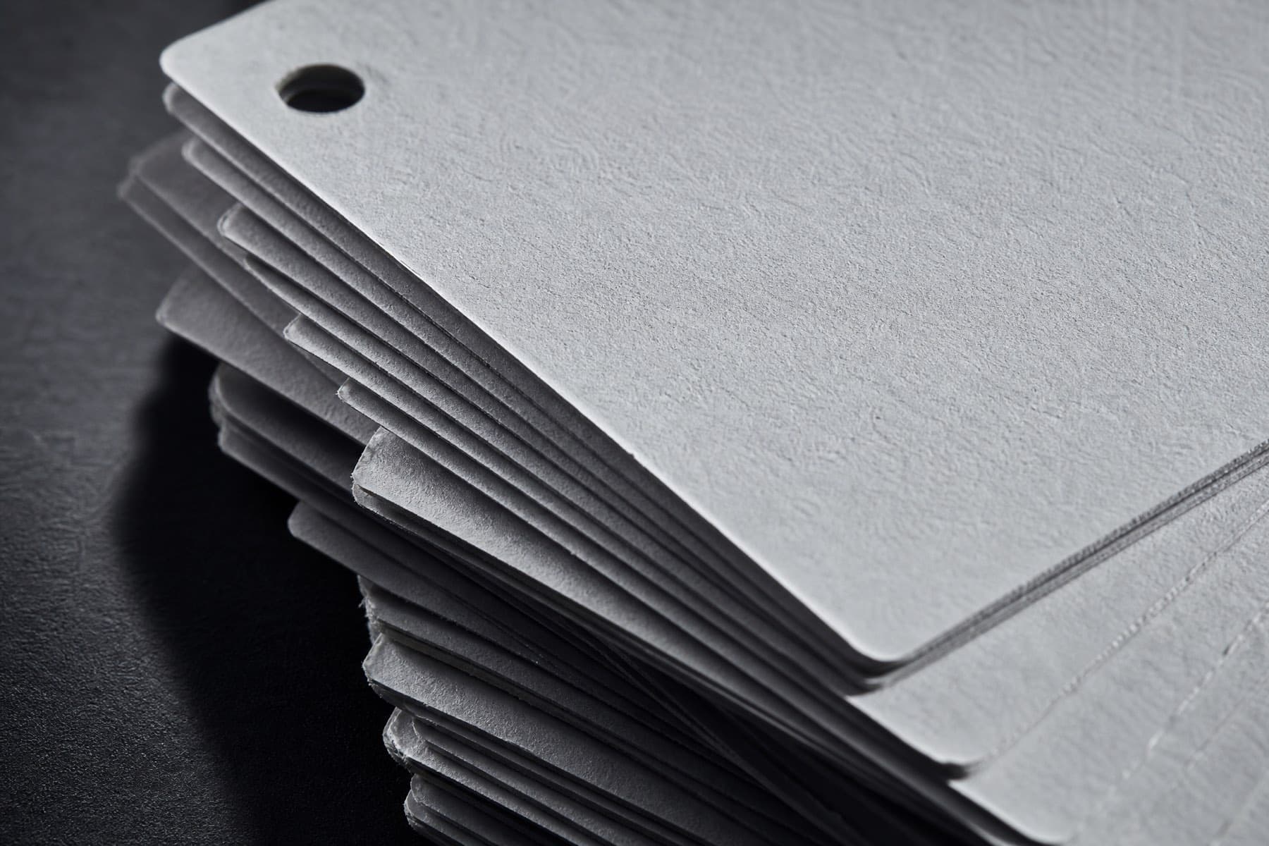 A stack of blank card hangtags on a dark surface, lit from one side