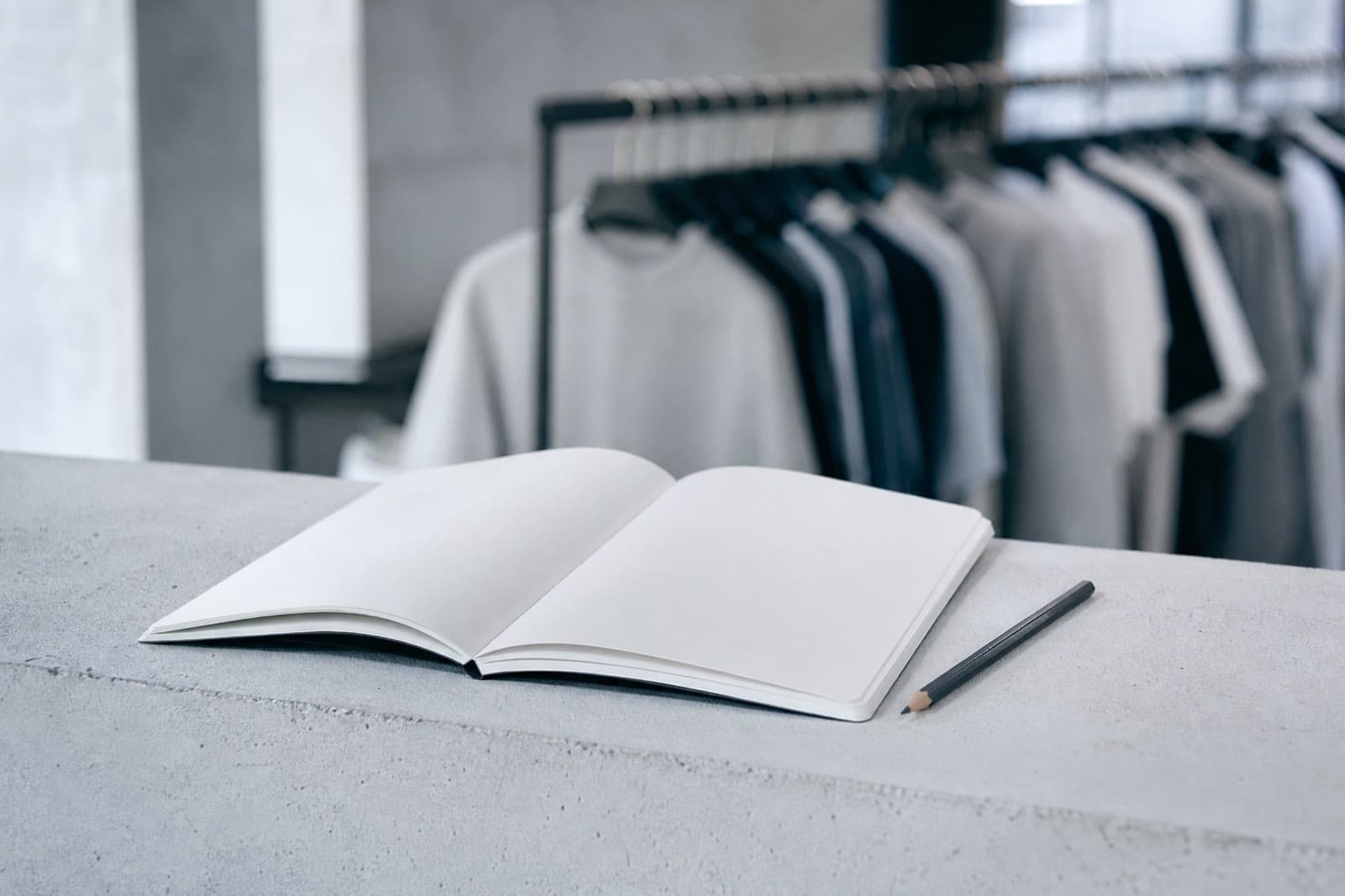 A blank notebook and pencil in front of a clothing rail